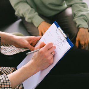 Personne prenant des notes et écoutant une seconde personne, illustrant une séance de mentorat des associations